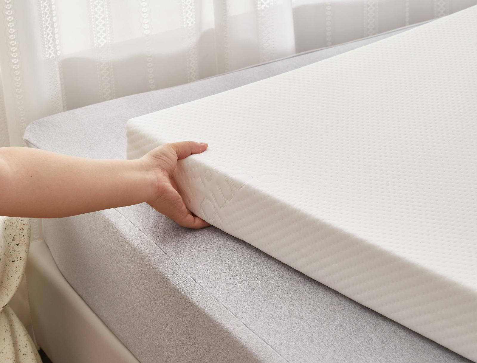 Person holding a mattress topper on a bed with white curtains in the background